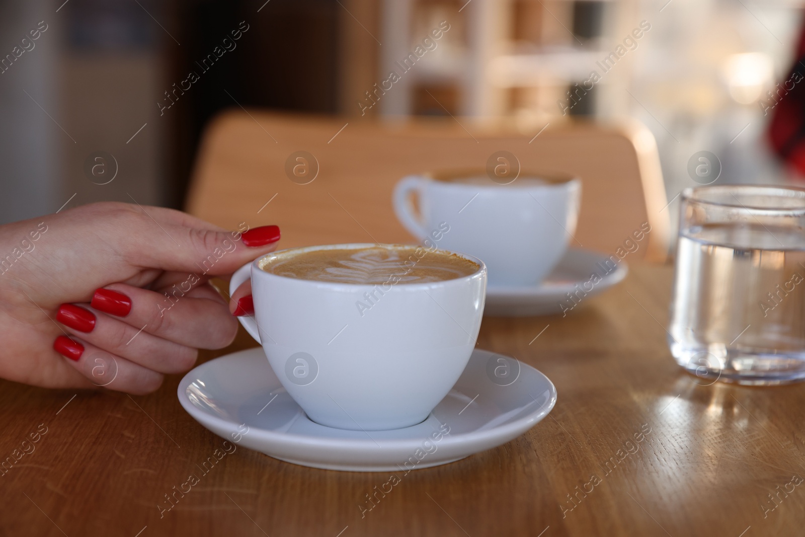 Photo of Woman with cup of aromatic coffee at wooden table in cafe, closeup