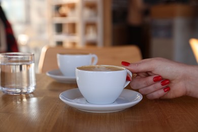 Photo of Woman with cup of aromatic coffee at wooden table in cafe, closeup