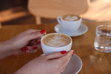 Photo of Woman with cup of aromatic coffee at wooden table in cafe, closeup