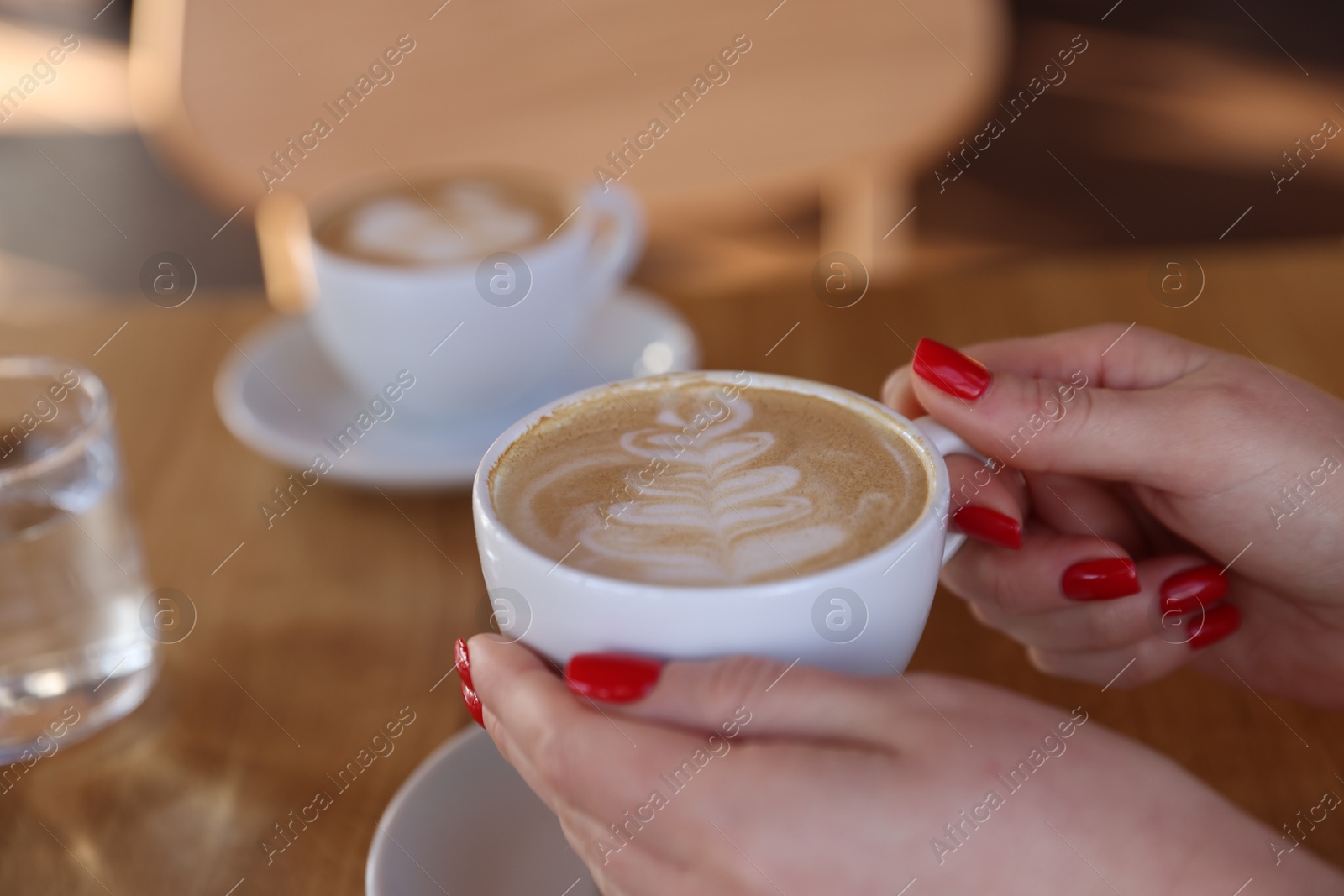 Photo of Woman with cup of aromatic coffee at table in cafe, closeup