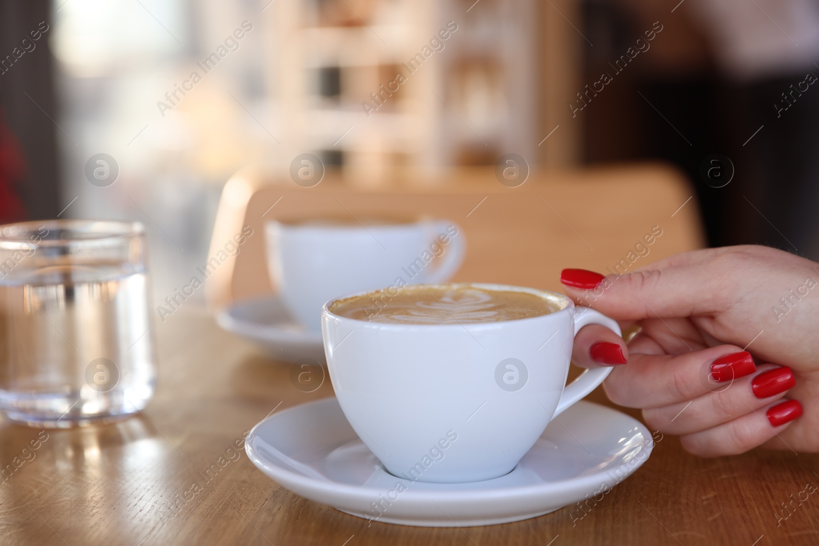 Photo of Woman with cup of aromatic coffee at wooden table in cafe, closeup