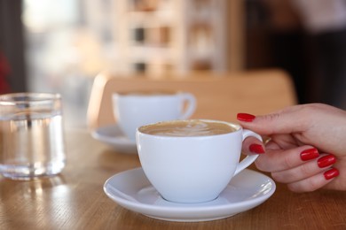 Photo of Woman with cup of aromatic coffee at wooden table in cafe, closeup