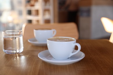 Photo of Cups of aromatic coffee and glass with water on wooden table in cafe, closeup