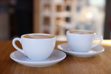 Photo of Cups of aromatic coffee on wooden table in cafe, closeup