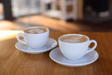 Photo of Cups of aromatic coffee on wooden table in cafe, closeup