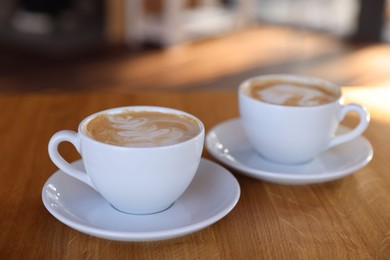 Photo of Cups of aromatic coffee on wooden table in cafe, closeup