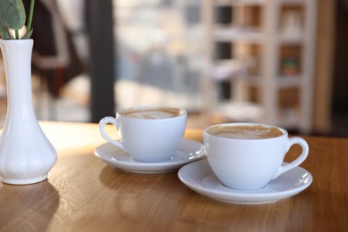 Photo of Cups of aromatic coffee on wooden table in cafe, closeup