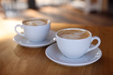 Photo of Cups of aromatic coffee on wooden table in cafe, closeup