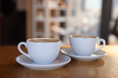 Photo of Cups of aromatic coffee on wooden table in cafe, closeup