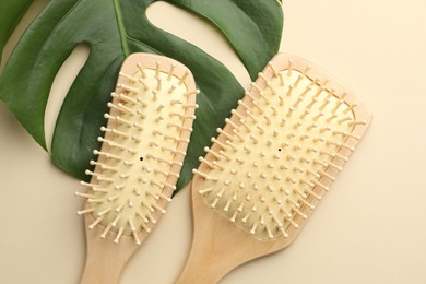 Photo of Wooden hair brushes and monstera leaf on beige background, flat lay