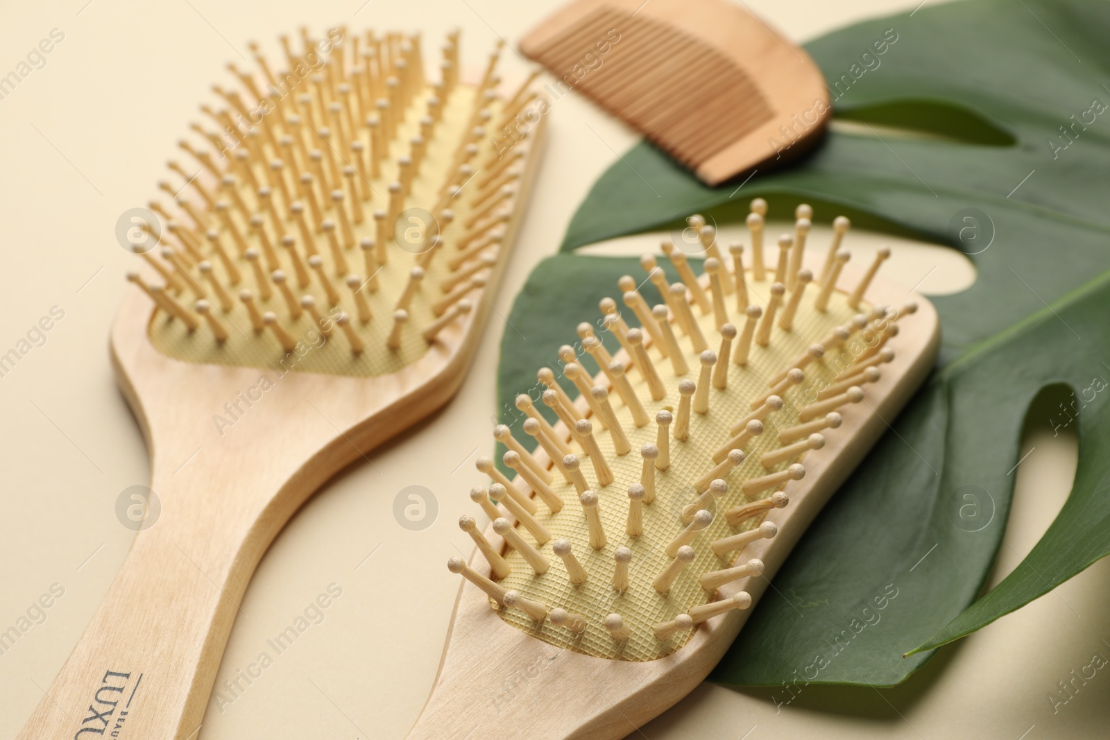 Photo of Wooden hair brushes, comb and monstera leaf on beige background, closeup