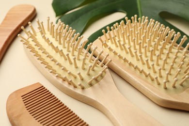 Photo of Wooden hair brushes, comb and monstera leaf on beige background, closeup