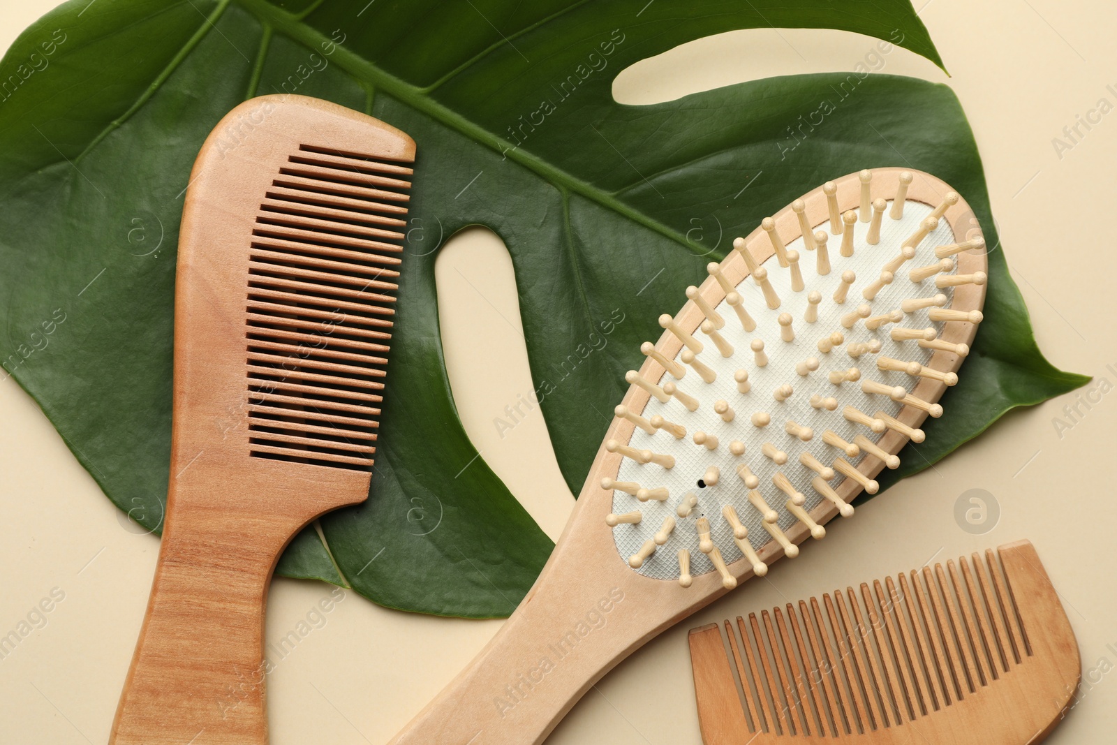 Photo of Wooden hair brush, combs and monstera leaf on beige background, flat lay