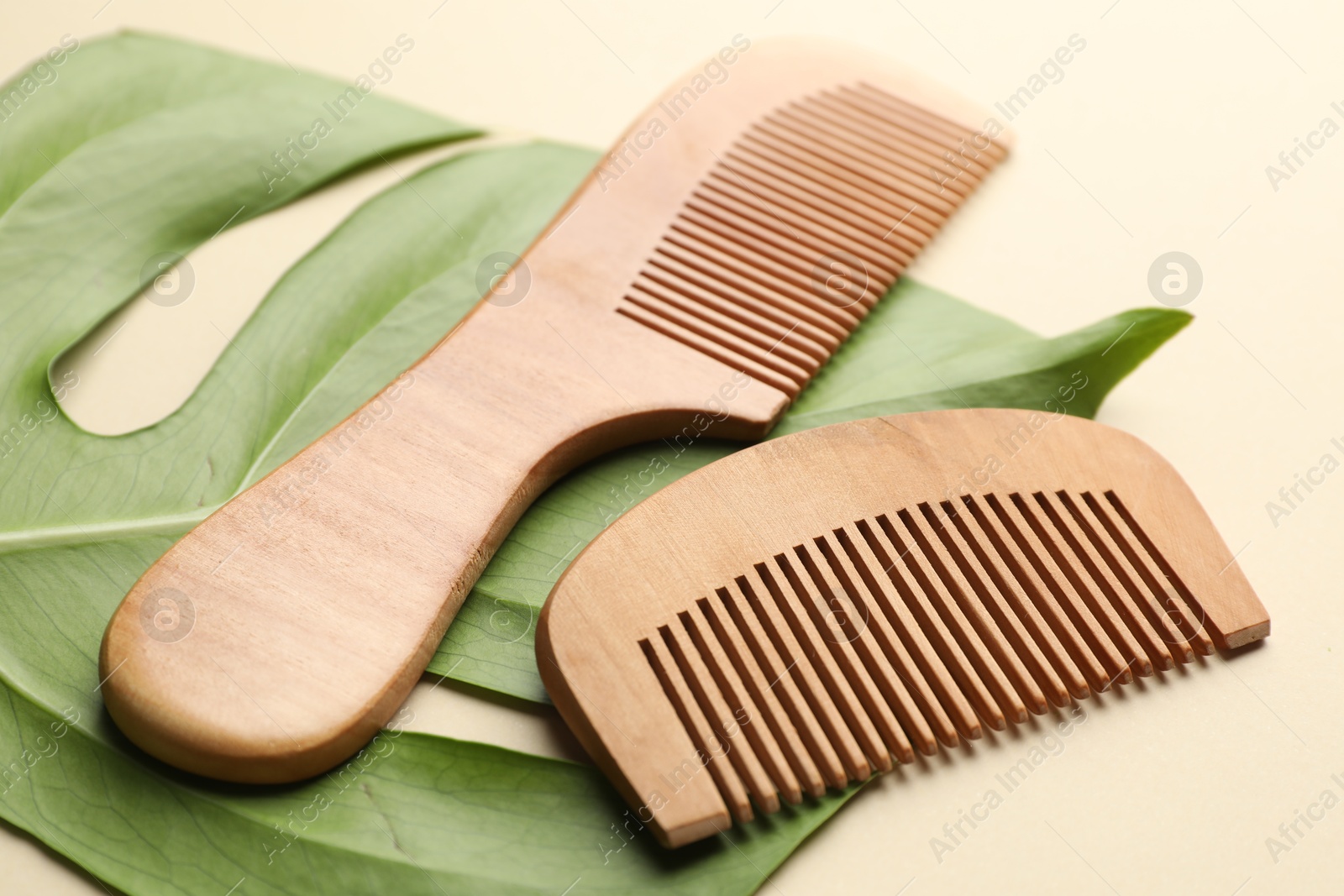 Photo of Wooden hair combs and monstera leaf on beige background, closeup