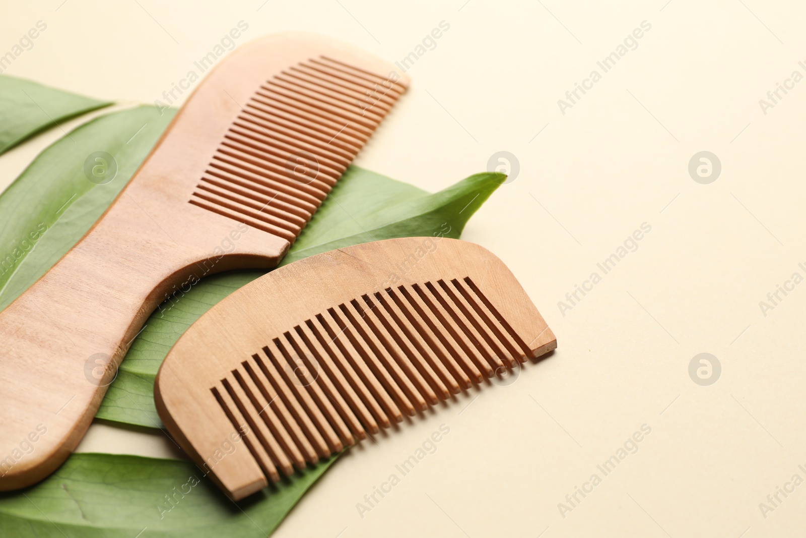 Photo of Wooden hair combs and monstera leaf on beige background, closeup. Space for text