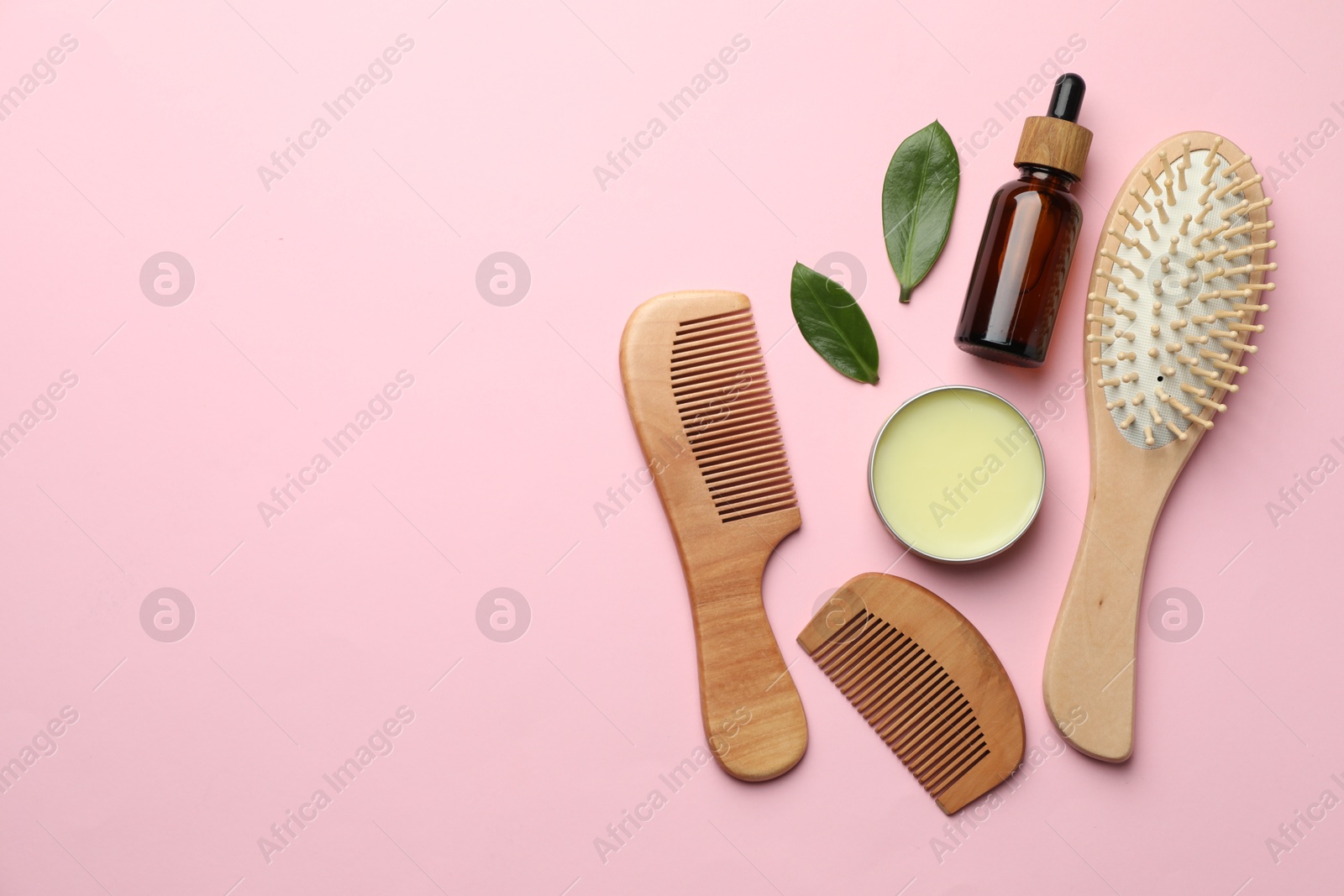 Photo of Wooden hair brush, combs, cosmetic products and green leaves on pink background, flat lay. Space for text