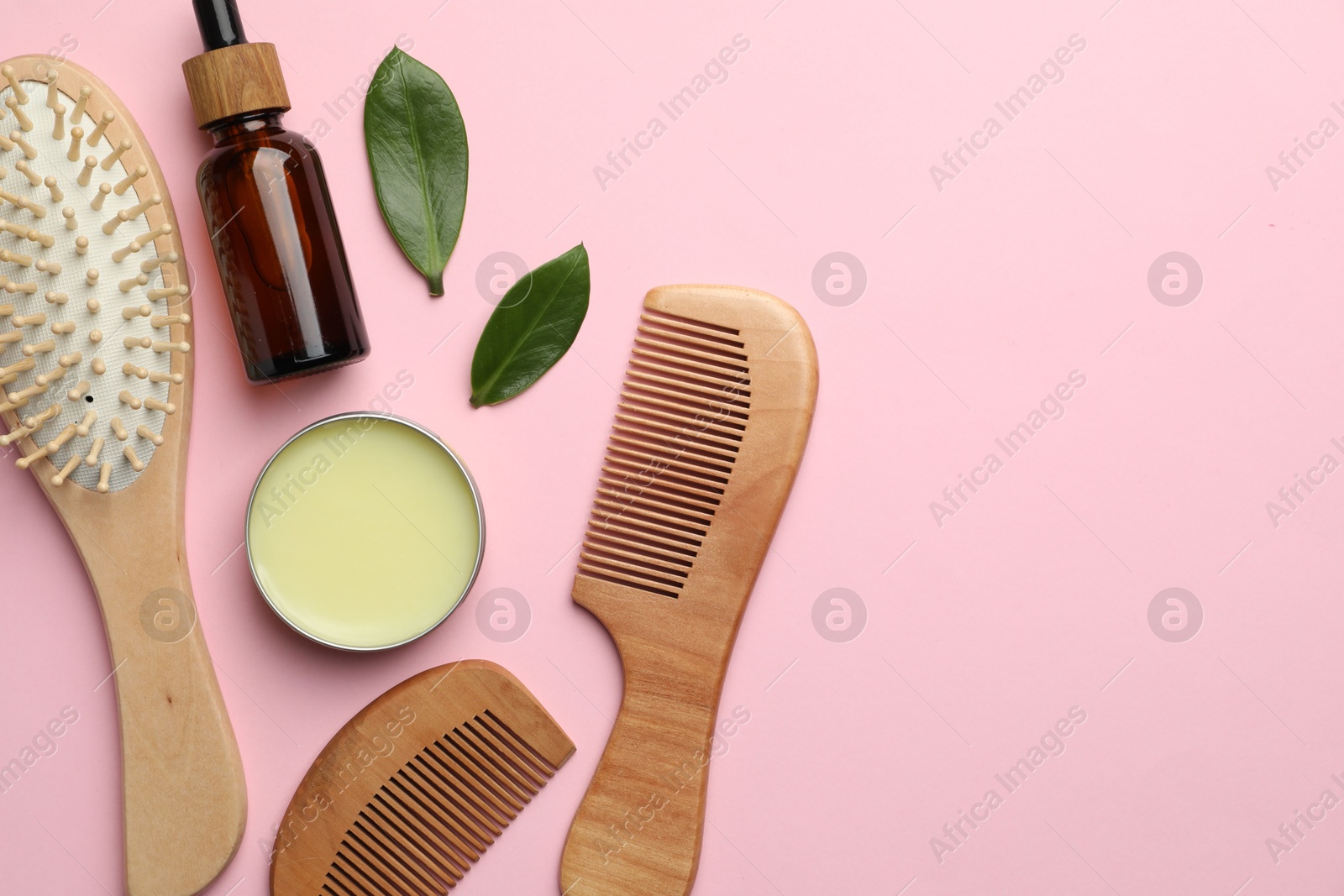 Photo of Wooden hair brush, combs, cosmetic products and green leaves on pink background, flat lay. Space for text