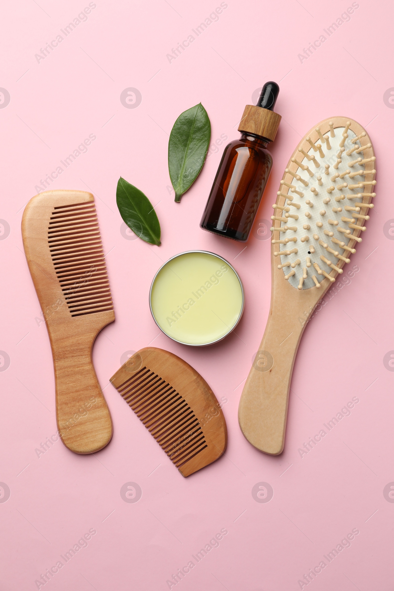 Photo of Wooden hair brush, combs, cosmetic products and green leaves on pink background, flat lay