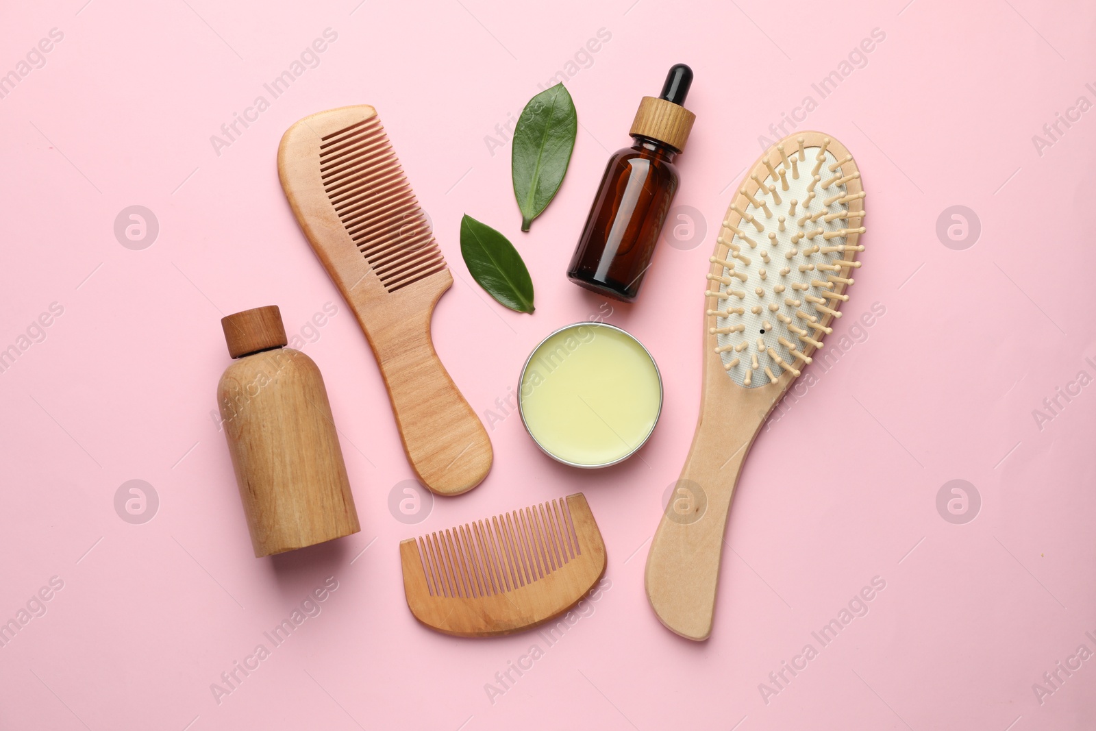 Photo of Wooden hair brush, combs, cosmetic products and green leaves on pink background, flat lay