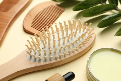 Photo of Wooden hair brush, combs, cosmetic products and green branch on beige background, closeup