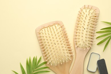 Photo of Wooden hair brushes, wax and green leaves on beige background, flat lay