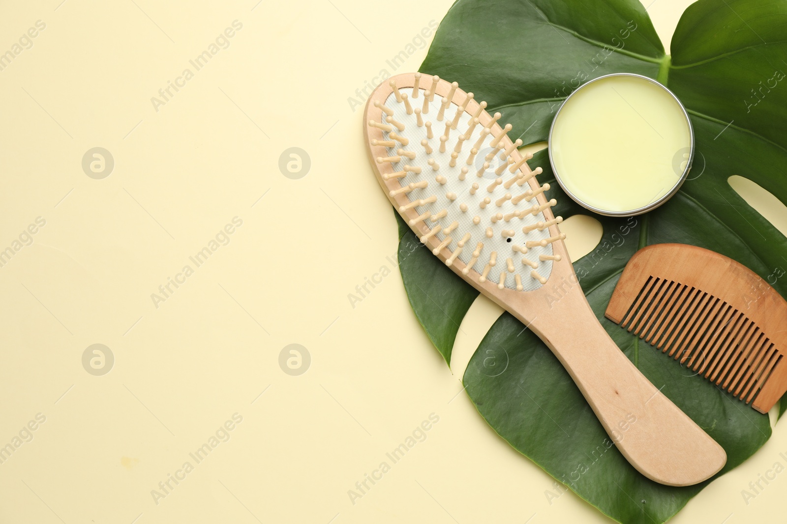 Photo of Wooden hair brush, comb, wax and monstera leaf on beige background, flat lay. Space for text