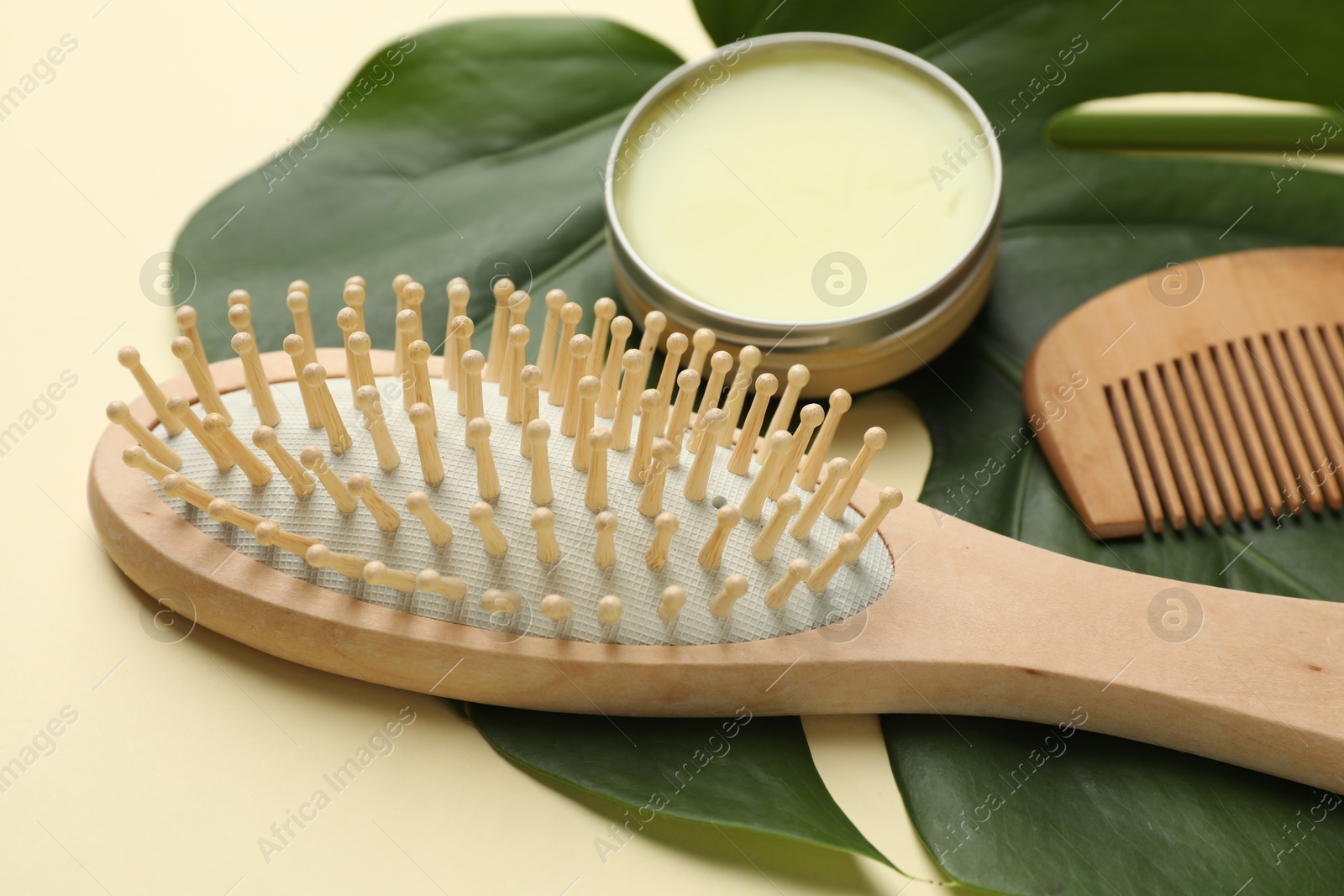 Photo of Wooden hair brush, comb, wax and monstera leaf on beige background, closeup