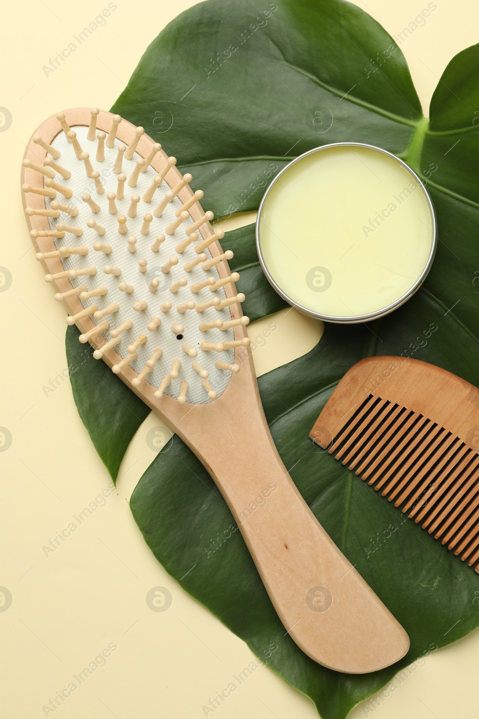 Photo of Wooden hair brush, comb, wax and monstera leaf on beige background, flat lay