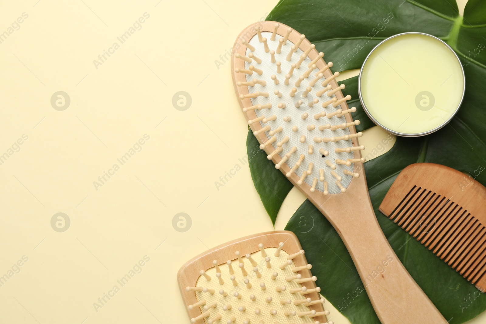 Photo of Wooden hair brushes, comb, wax and monstera leaf on beige background, flat lay. Space for text