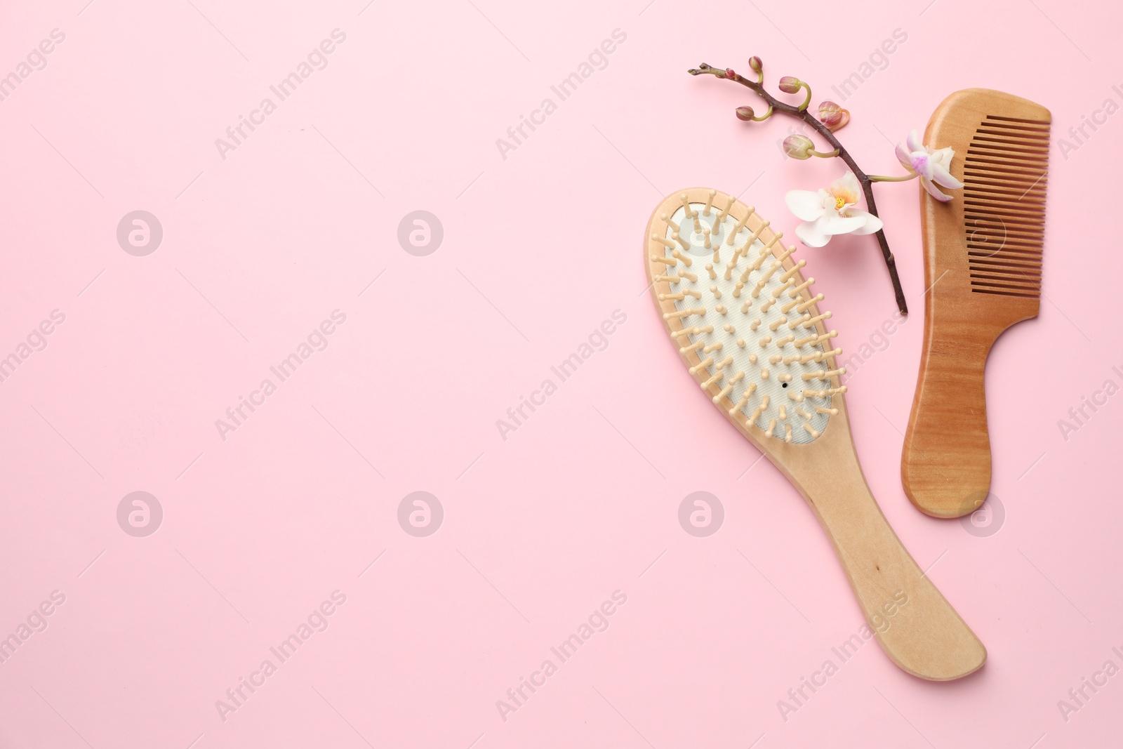 Photo of Wooden hair brush, comb and orchid branch on pink background, flat lay. Space for text