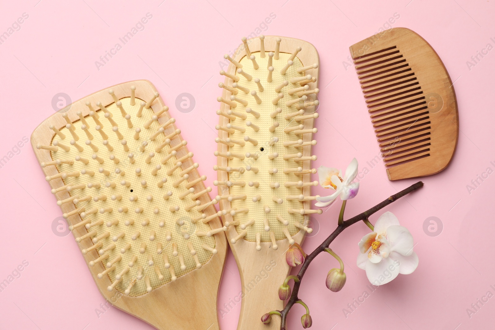 Photo of Wooden hair brushes, comb and orchid branch on pink background, flat lay