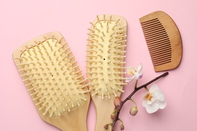 Photo of Wooden hair brushes, comb and orchid branch on pink background, flat lay