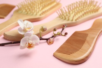 Photo of Wooden hair brushes, comb and orchid branch on pink background, closeup