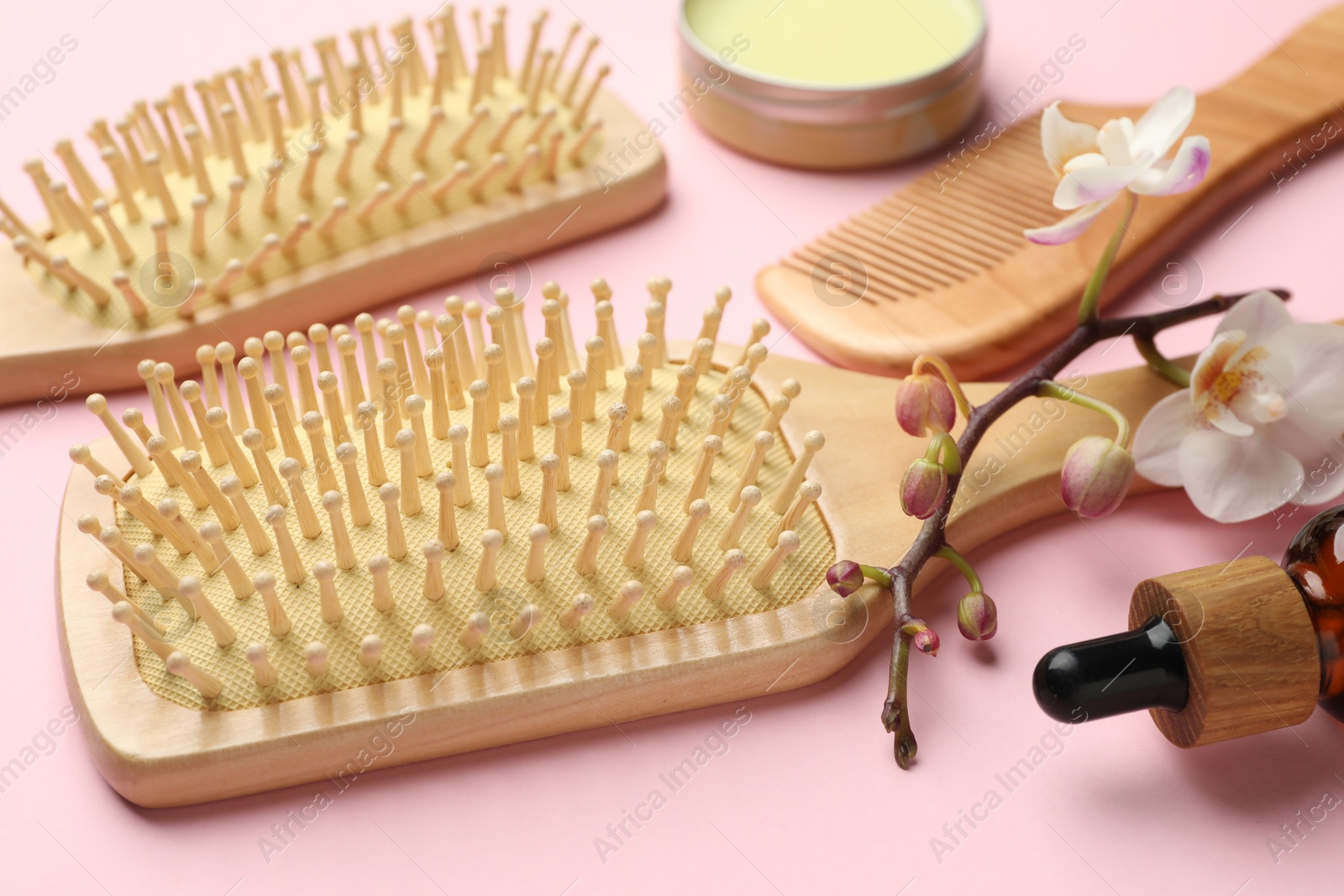 Photo of Wooden hair brushes, comb, cosmetic products and orchid branch on pink background, closeup