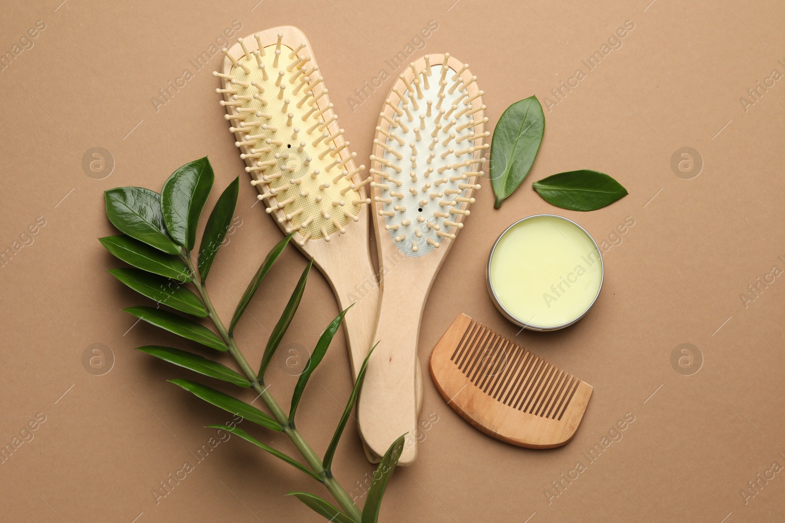 Photo of Wooden hair brushes, comb, wax and green branch on dark beige background, flat lay