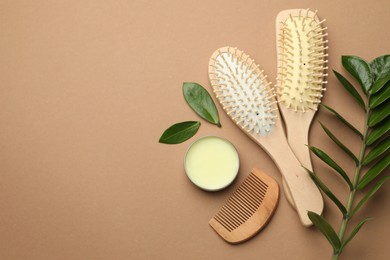 Photo of Wooden hair brushes, comb, wax and green branch on dark beige background, flat lay. Space for text