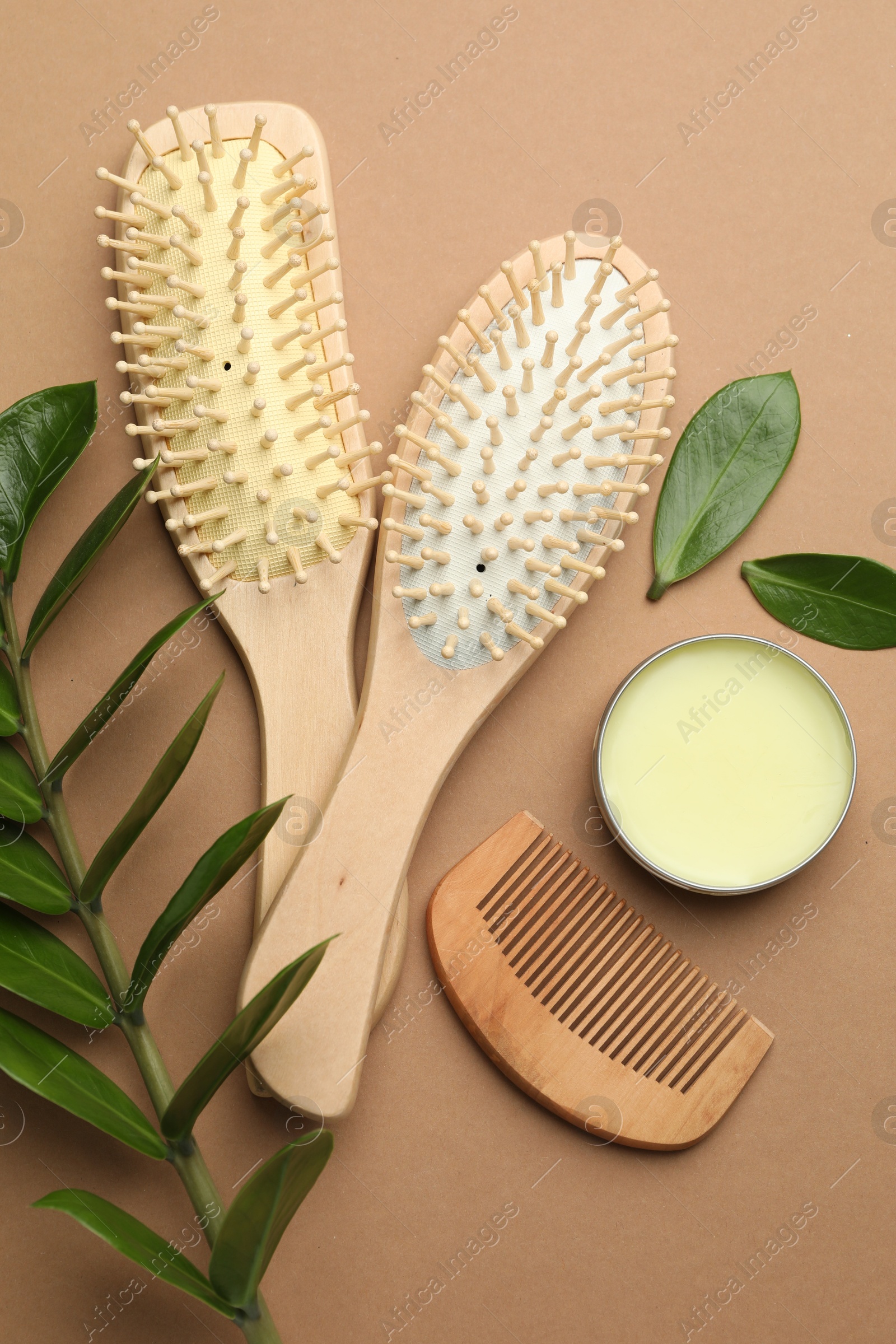 Photo of Wooden hair brushes, comb, wax and green branch on dark beige background, flat lay