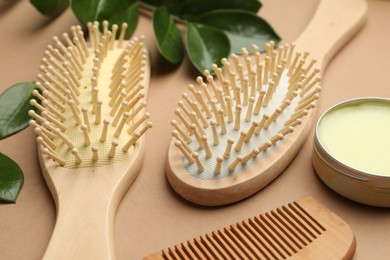 Photo of Wooden hair brushes, comb, wax and green leaves on dark beige background, closeup