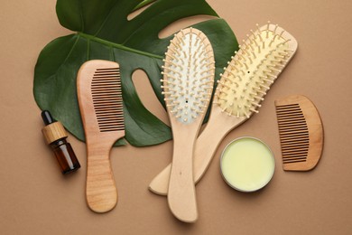 Photo of Wooden hair brushes, combs, cosmetic products and monstera leaf on dark beige background, flat lay