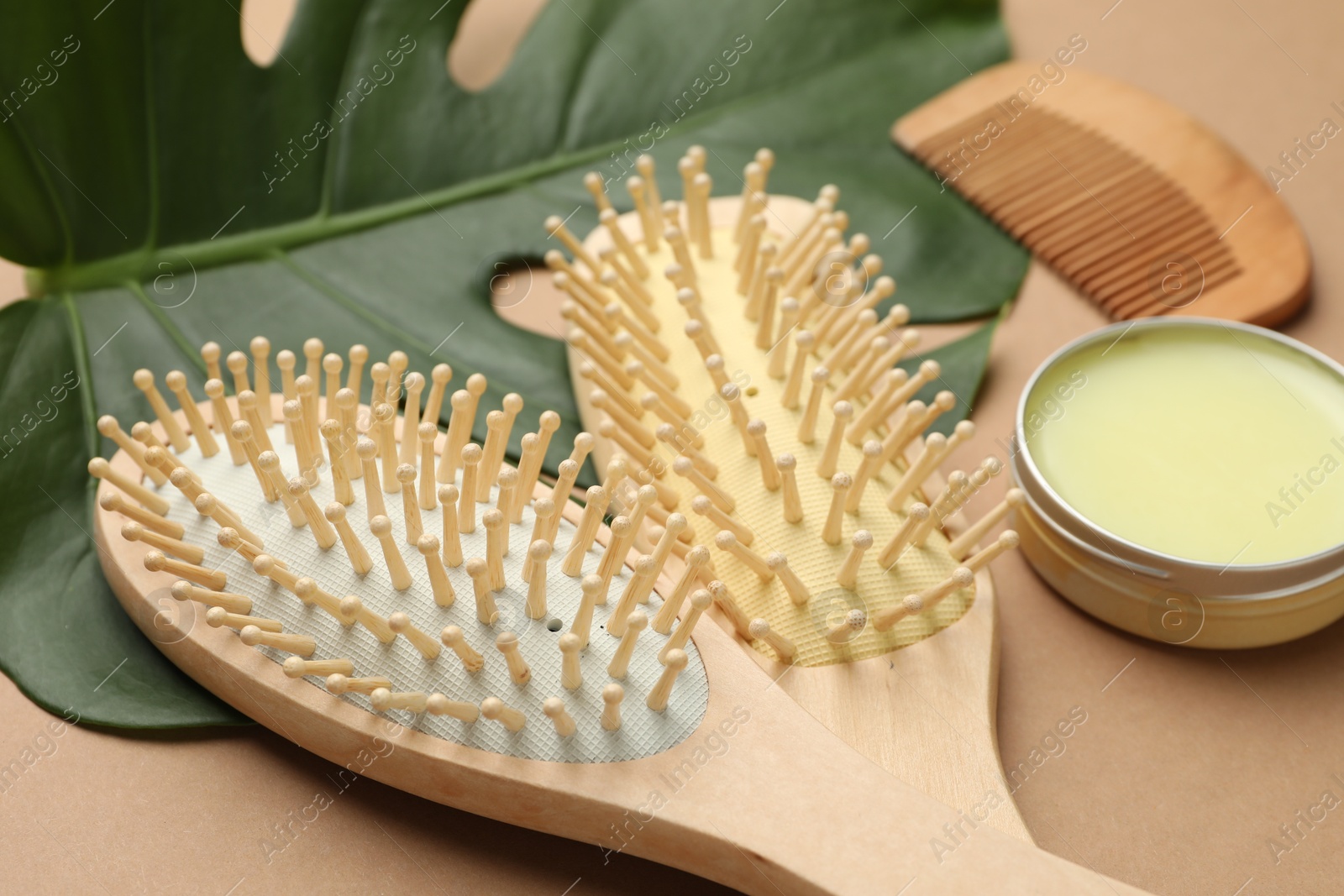 Photo of Wooden hair brushes, wax, comb and monstera leaf on dark beige background, closeup