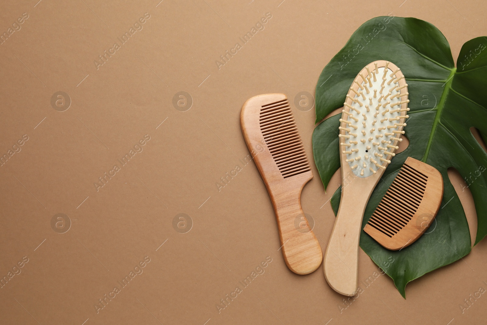 Photo of Wooden hair brush, combs and monstera leaf on dark beige background, flat lay. Space for text