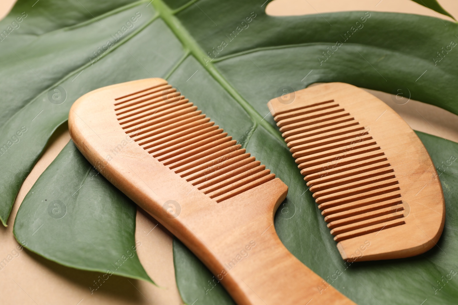 Photo of Wooden hair brush, comb and monstera leaf on dark beige background, closeup