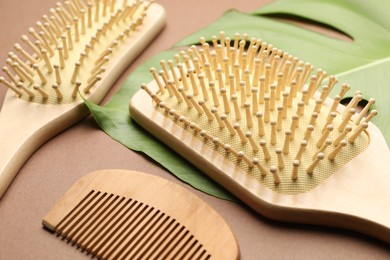 Photo of Wooden hair brushes, comb and monstera leaf on dark beige background, closeup