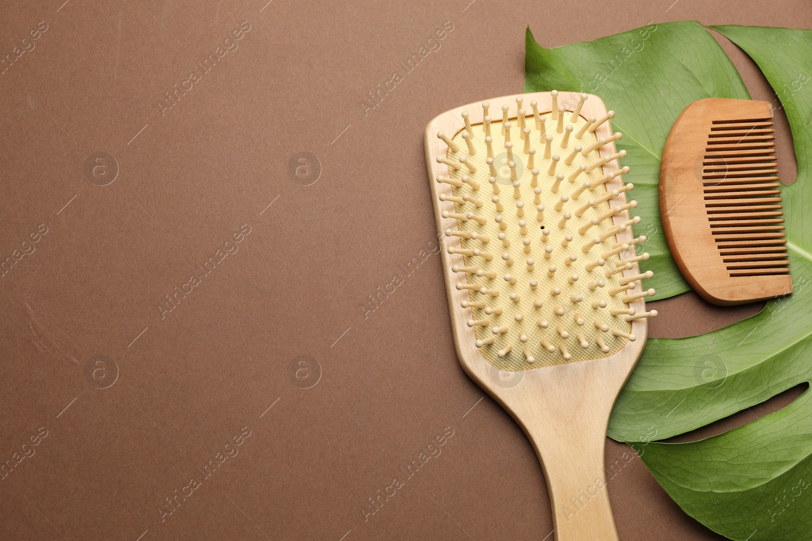 Photo of Wooden hair brush, comb and monstera leaf on dark beige background, flat lay. Space for text