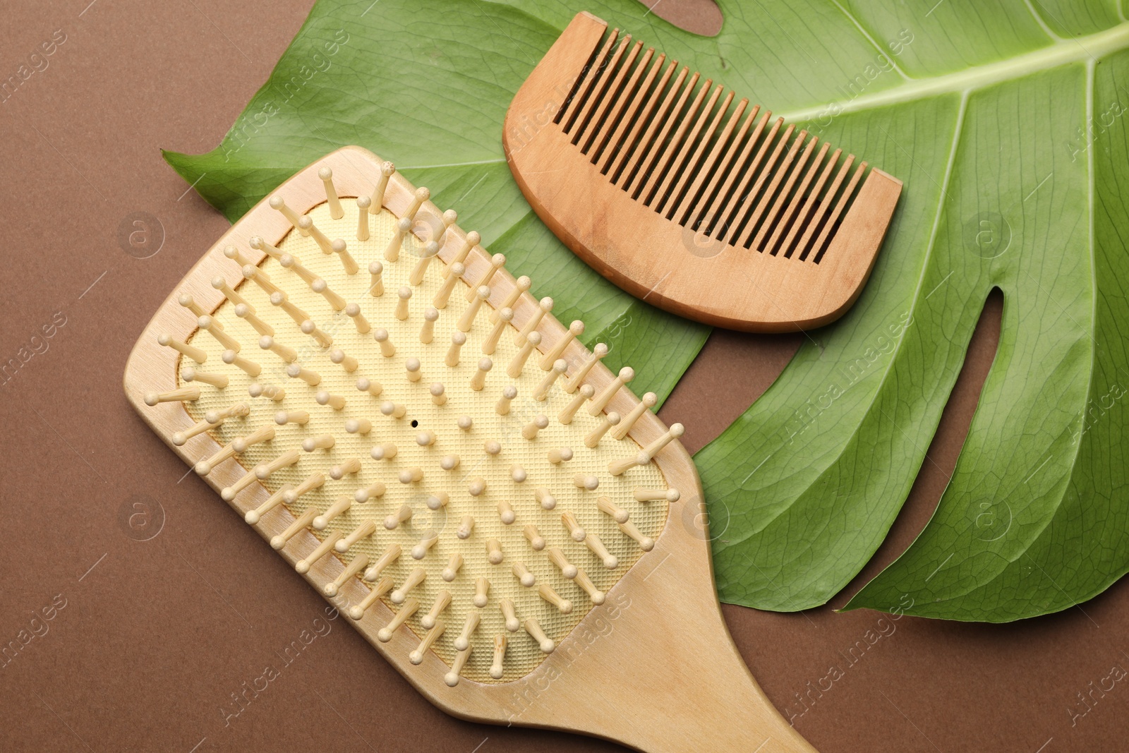 Photo of Wooden hair brush, comb and monstera leaf on dark beige background, flat lay