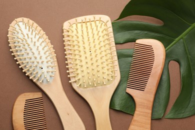 Photo of Wooden hair brushes, combs and monstera leaf on dark beige background, flat lay