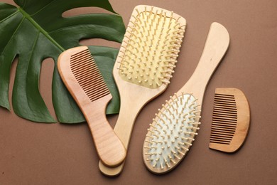 Photo of Wooden hair brushes, combs and monstera leaf on dark beige background, flat lay