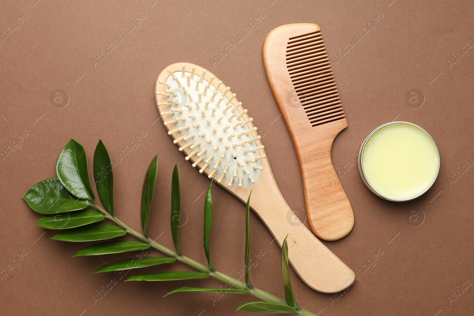 Photo of Wooden hair brush, comb, wax and green branch on dark beige background, flat lay