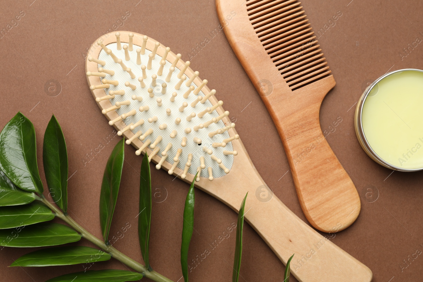 Photo of Wooden hair brush, comb, wax and green branch on dark beige background, flat lay