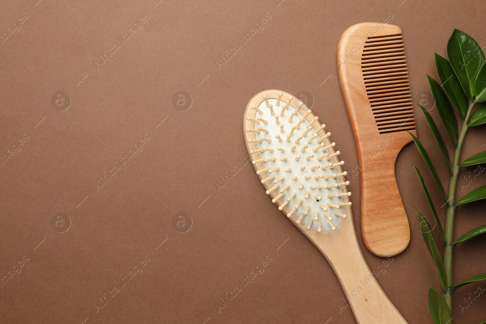 Photo of Wooden hair brush, comb and green branch on dark beige background, flat lay. Space for text